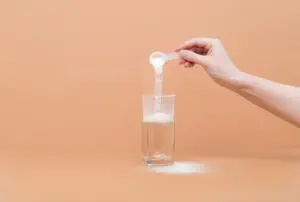 Woman pours collagen powder or&nbsp;protein in&nbsp;a&nbsp;glass of water on&nbsp;a&nbsp;beige background. A&nbsp;healthy and anti aging supplement.